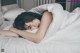 A woman laying in bed under a white blanket.