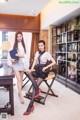 A couple of women sitting on top of a wooden chair.