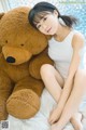 A woman sitting on a bed next to a large teddy bear.