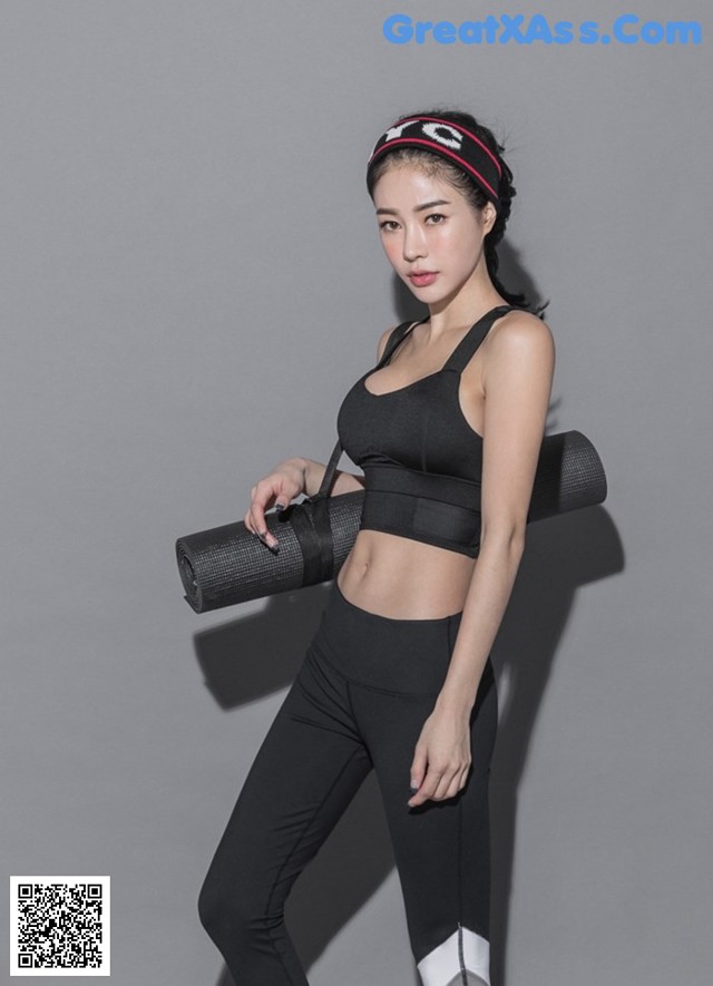 A woman in a black sports bra top and black leggings holding a yoga mat.