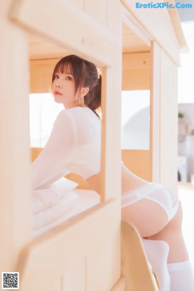 A woman in a white shirt and white stockings sitting on a bed.