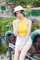 A woman in a yellow tank top and white shorts posing next to a bike.