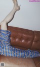 A woman is sitting on a brown couch with her legs up.