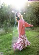 A woman in a pink sweater and a floral skirt is dancing in the grass.