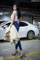 A woman standing in front of a white car in a parking garage.