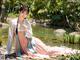 A woman in a pink and blue dress sitting by a pond.