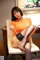 A woman in an orange top and black stockings sitting on a chair.