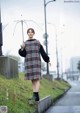 A woman in a plaid dress holding an umbrella on a sidewalk.