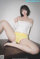 A woman in a white top and yellow panties sitting on a table.