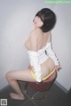 A woman in a white shirt and yellow panties sitting on a stool.