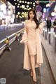 A woman in a pink dress and fur coat walking down the street.