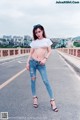 A woman in ripped jeans and a white t-shirt posing on a bridge.