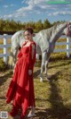 A woman in a red dress standing next to a white horse.