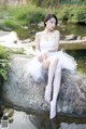 A woman in a white dress sitting on a rock by a river.