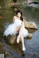 A woman in a white dress sitting on a rock in the water.