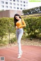 A woman in a yellow top and jeans standing on a wooden deck.