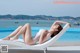 A woman in a white bathing suit laying on a lounge chair by a pool.