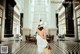 A woman in a white dress and hat walking through a lobby.