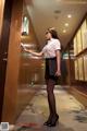 A woman in a white shirt and black skirt standing in an elevator.