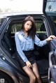 A woman in a blue shirt and black skirt sitting in a car.