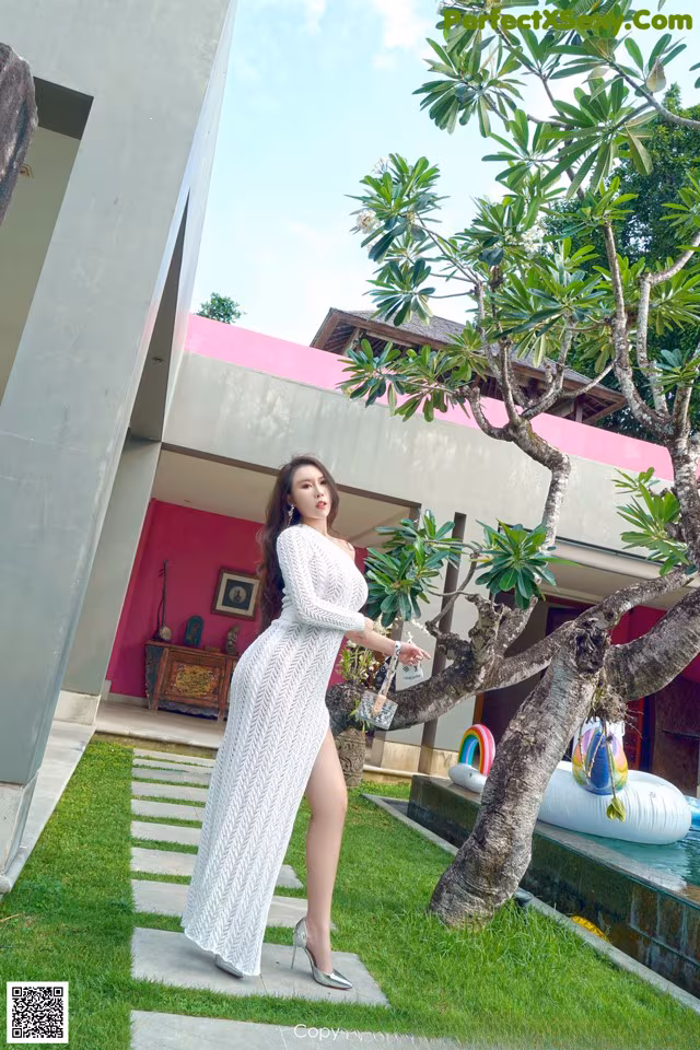 A woman in a white dress standing next to a tree.